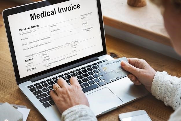 Person uses laptop showing a "Medical invoice" form on screen, typing to complete billing details.