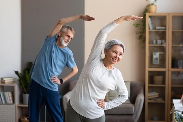 Smiling senior couple doing side stretches together at home to stay physically active.