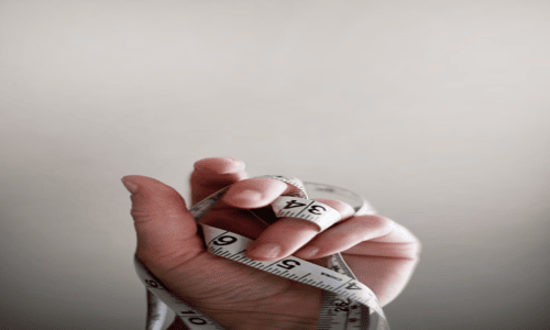 Hand holding a white flexible measuring tape coiled through the fingers.