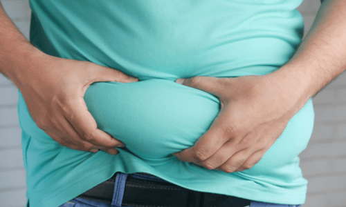 Person in a turquoise t-shirt holding and pinching excess belly fat with both hands.