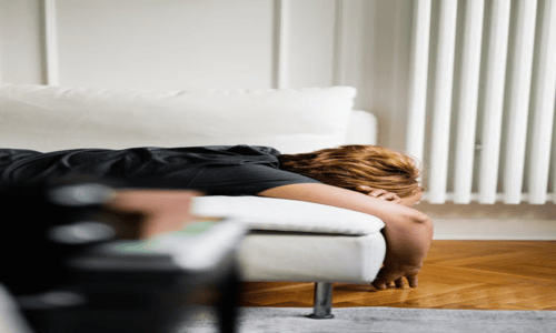 Person lying face down on a white sofa with an arm dangling toward the floor.  