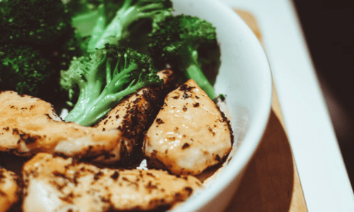 Bowl filled with seasoned grilled chicken breast pieces paired with steamed broccoli florets.